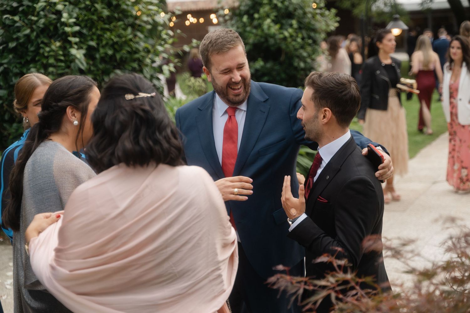 Wedding guests mingle and socialize during an outdoor reception under string lights.