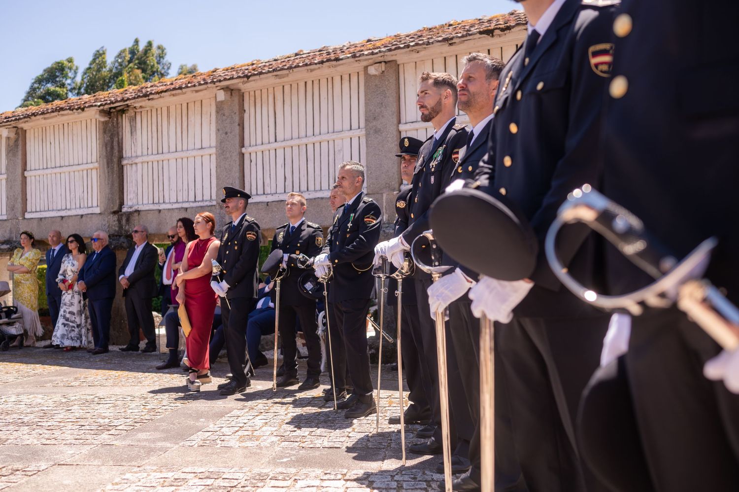 Musicians lined up with bagpipes at a traditional Galician festival in front of rustic white storage buildings.