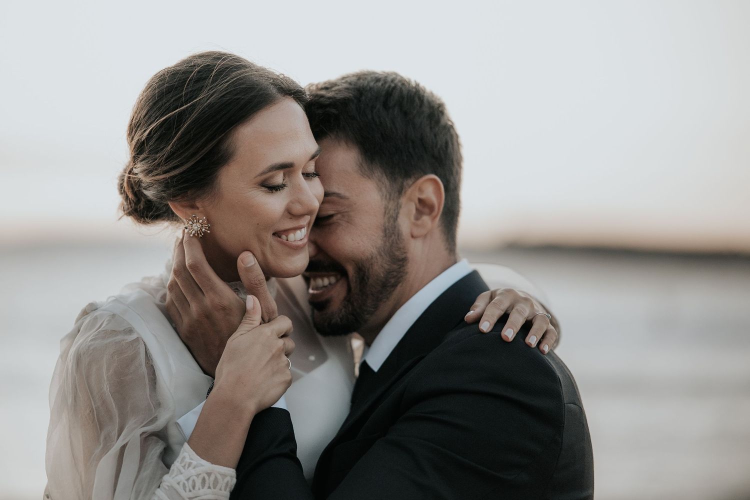 A couple shares an intimate moment while embracing and smiling together outdoors during golden hour.