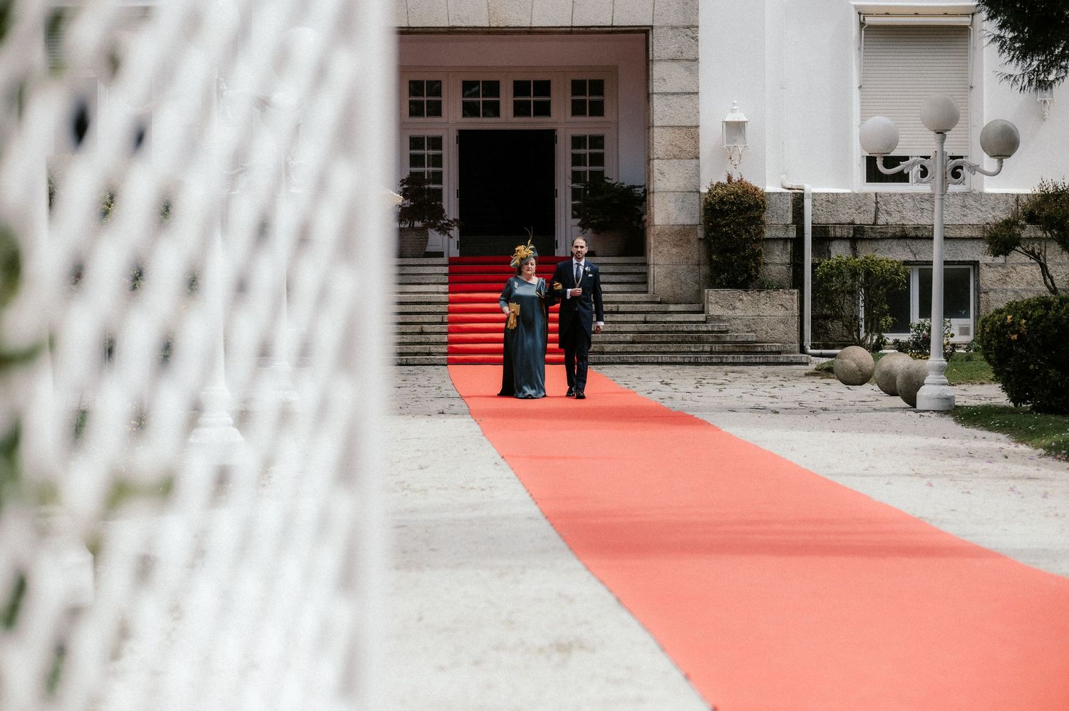 Red carpet leading up stone steps to entrance of grand building with white columns and glass doors.