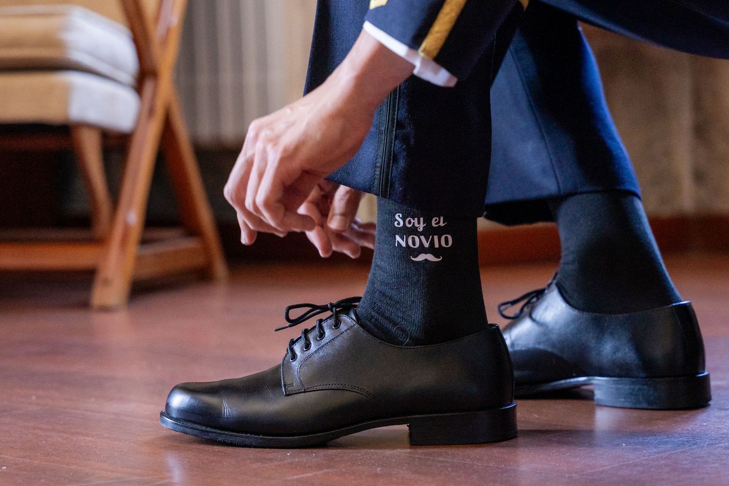 Black leather chelsea boots being put on feet while sitting on wooden floor.