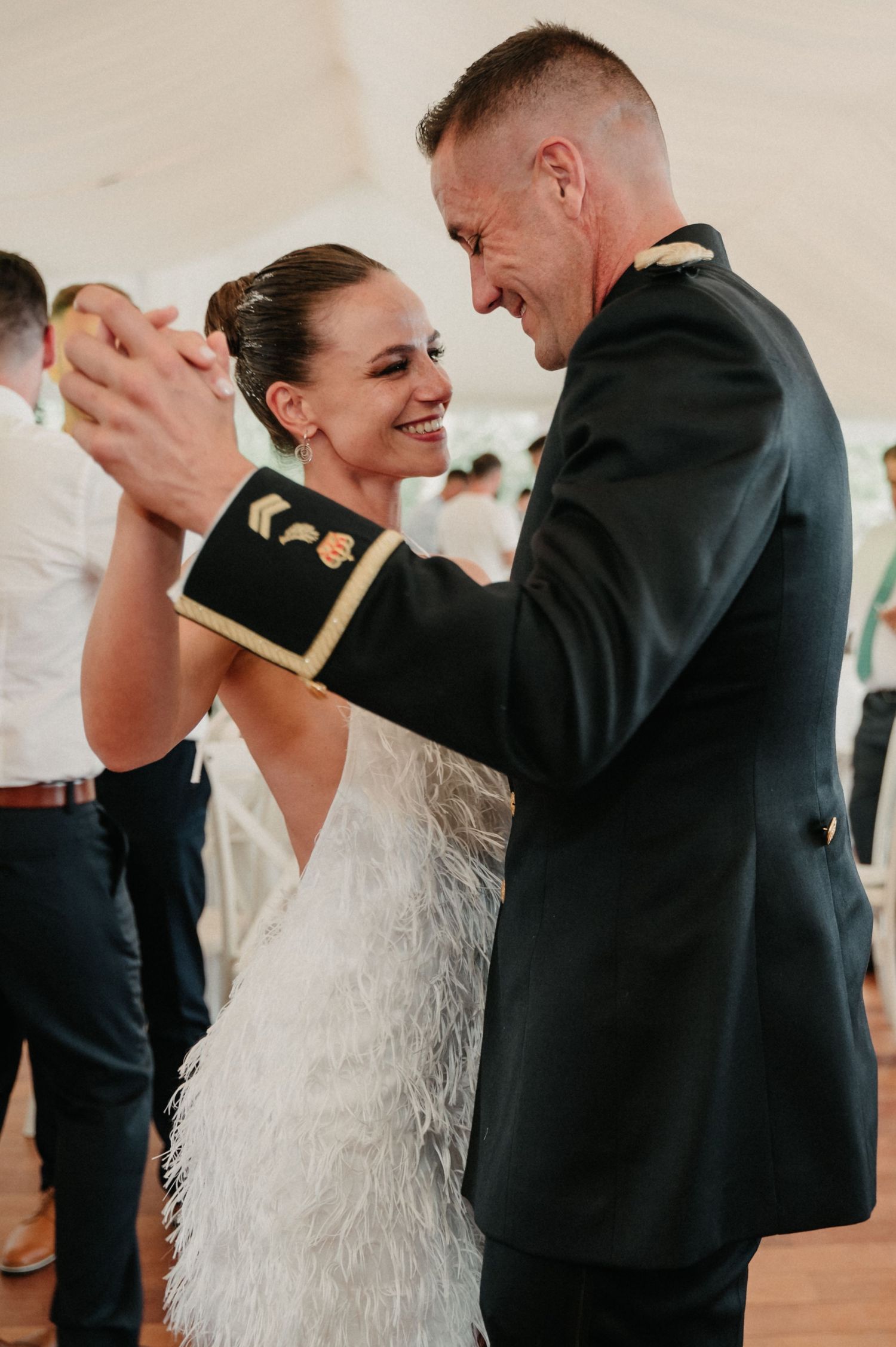 A couple shares a joyful dance together at their wedding reception, with the bride wearing a feathered white gown.