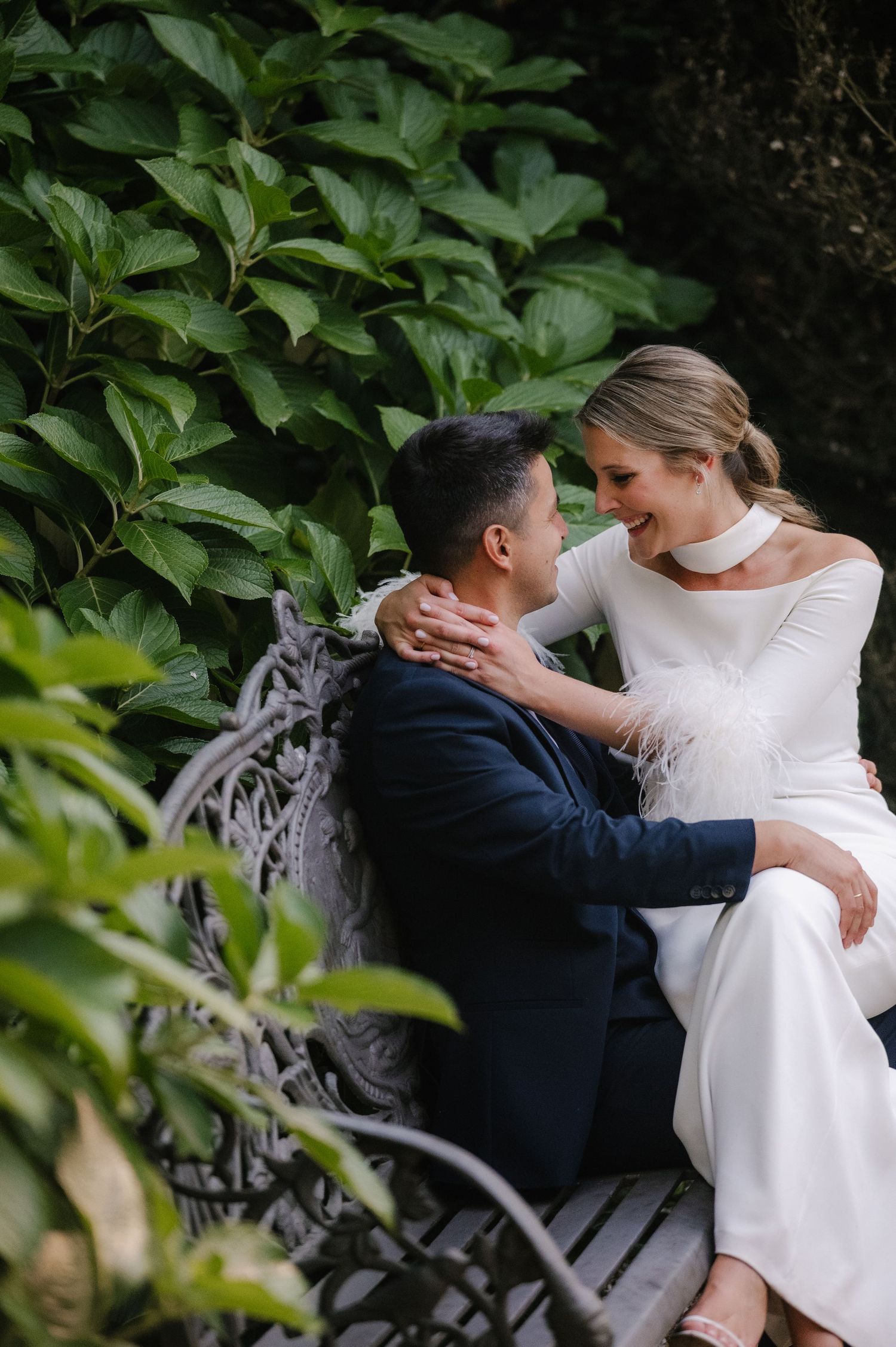 A romantic wedding moment captured in a lush garden setting with white dress and navy suit.