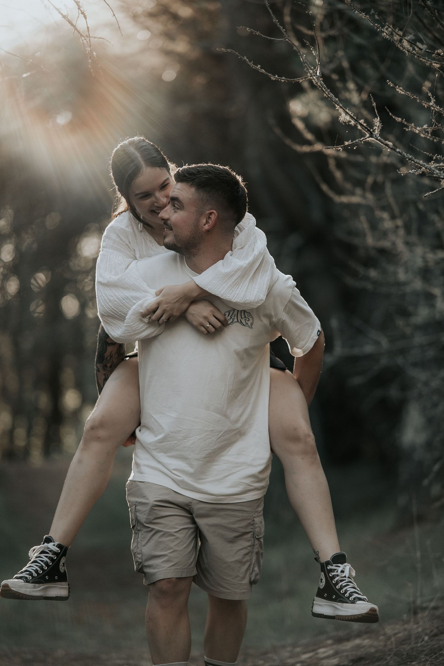 Couple in casual white outfits embrace playfully in a dimly lit outdoor setting.