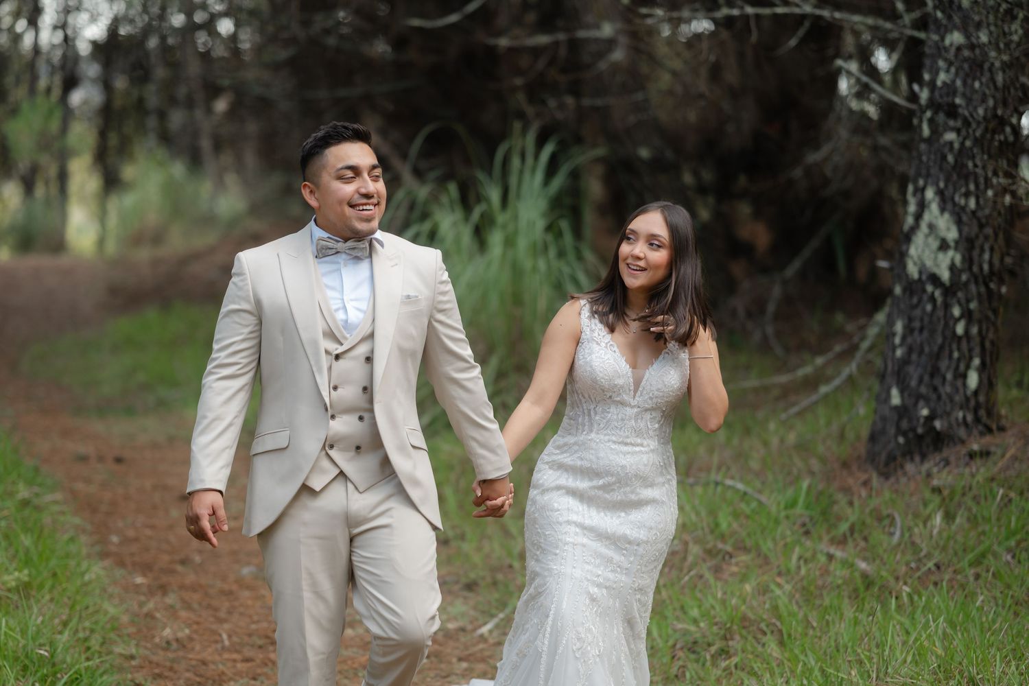 A couple in wedding attire walks hand in hand through a wooded path on their special day.