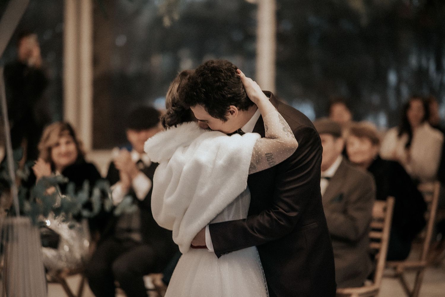 A couple shares their first dance at a wedding reception while guests look on in a dimly lit venue.