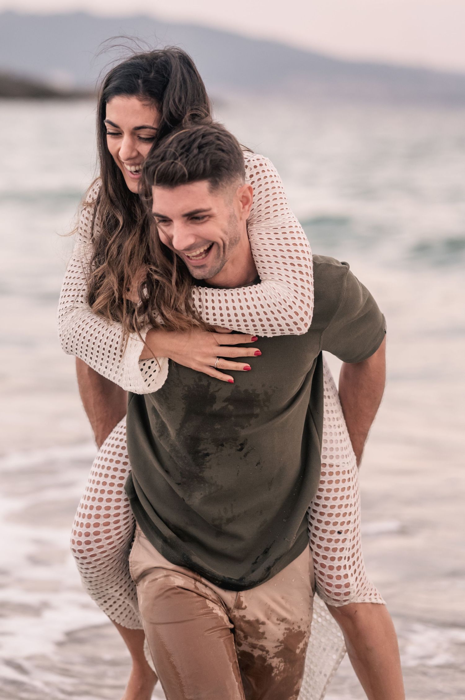 Playful piggyback ride on beach as couple laughs together during sunset.