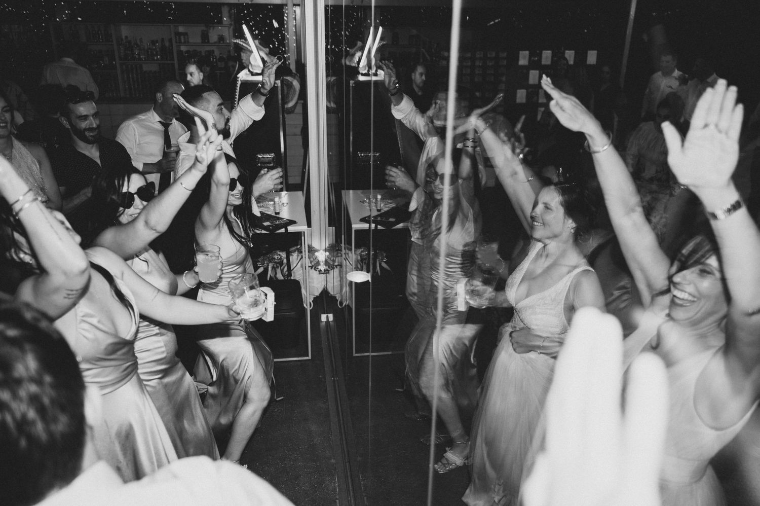 Black and white photo of people dancing with raised hands at what appears to be a party or celebration.