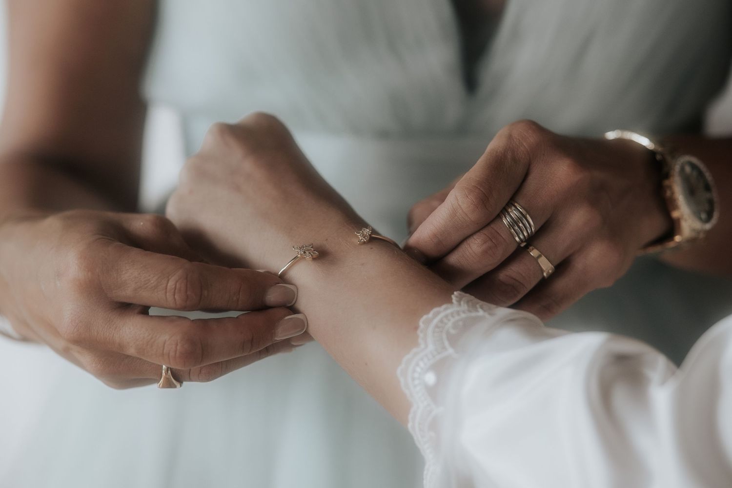 Close-up view of hands adjusting delicate white lace on a wedding dress sleeve.