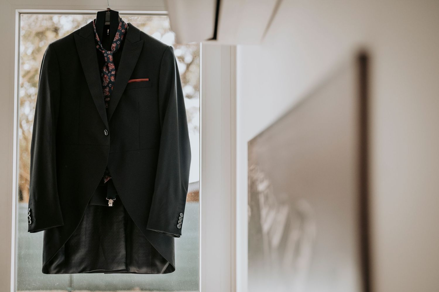 A black blazer jacket hanging on display against a light colored wall.
