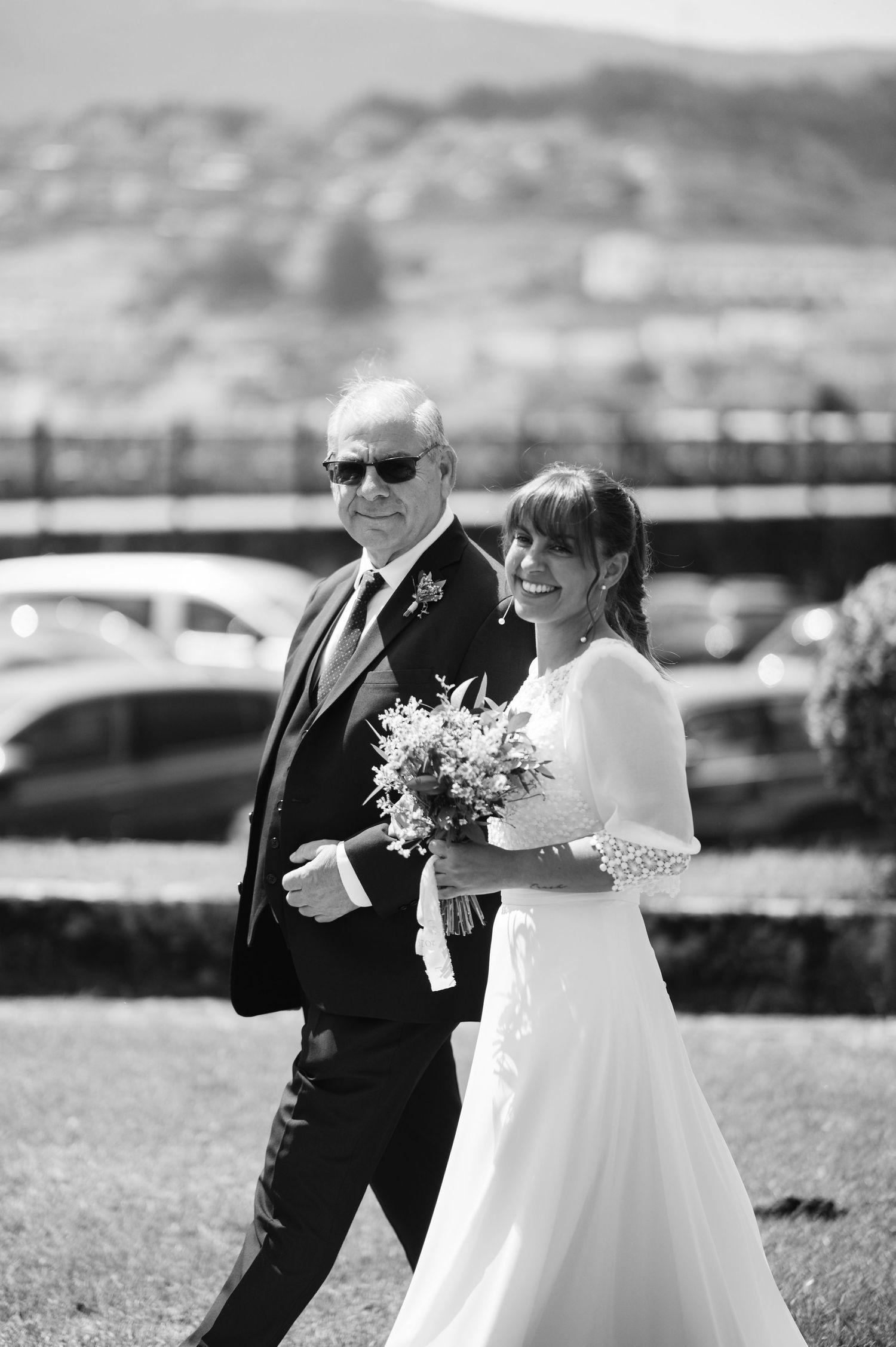Black and white wedding photo showing couple walking together outdoors with mountains in background.