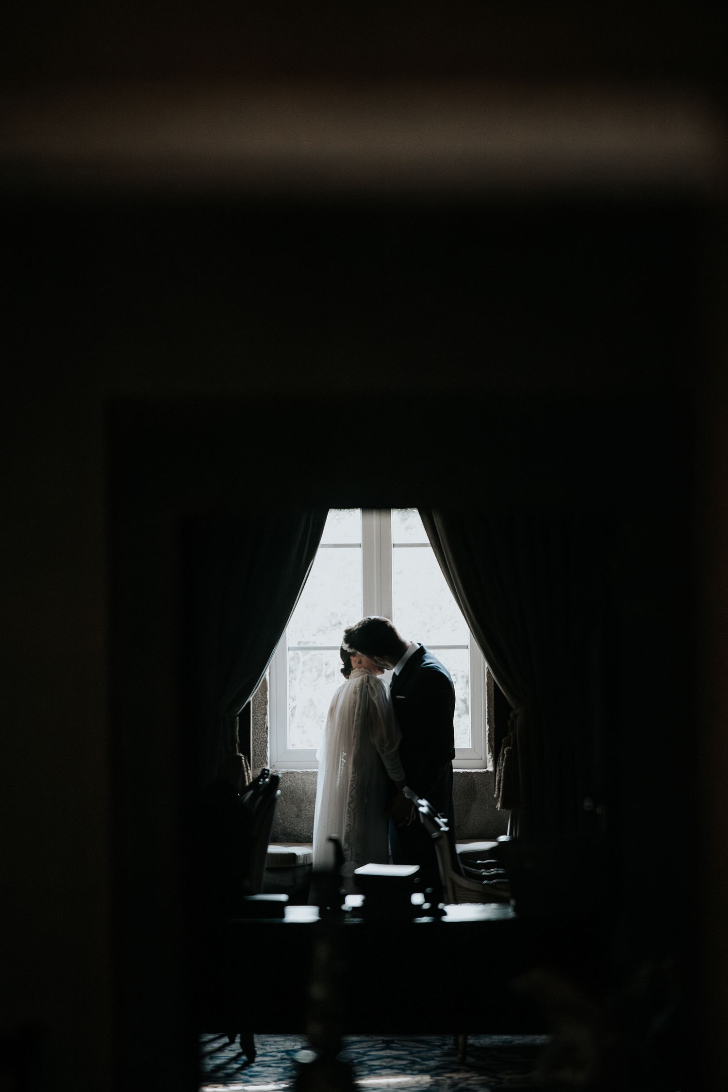 Dramatic silhouettes against window light in dimly lit interior space.