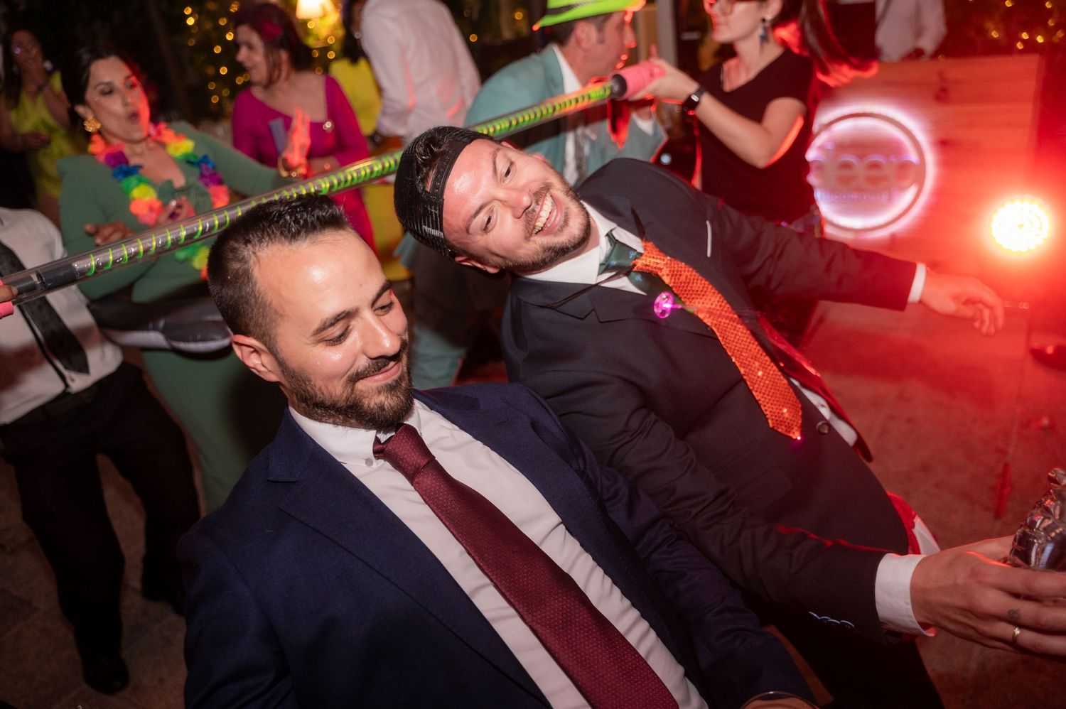 Wedding reception dance party with red lighting and guests dancing in formal attire.