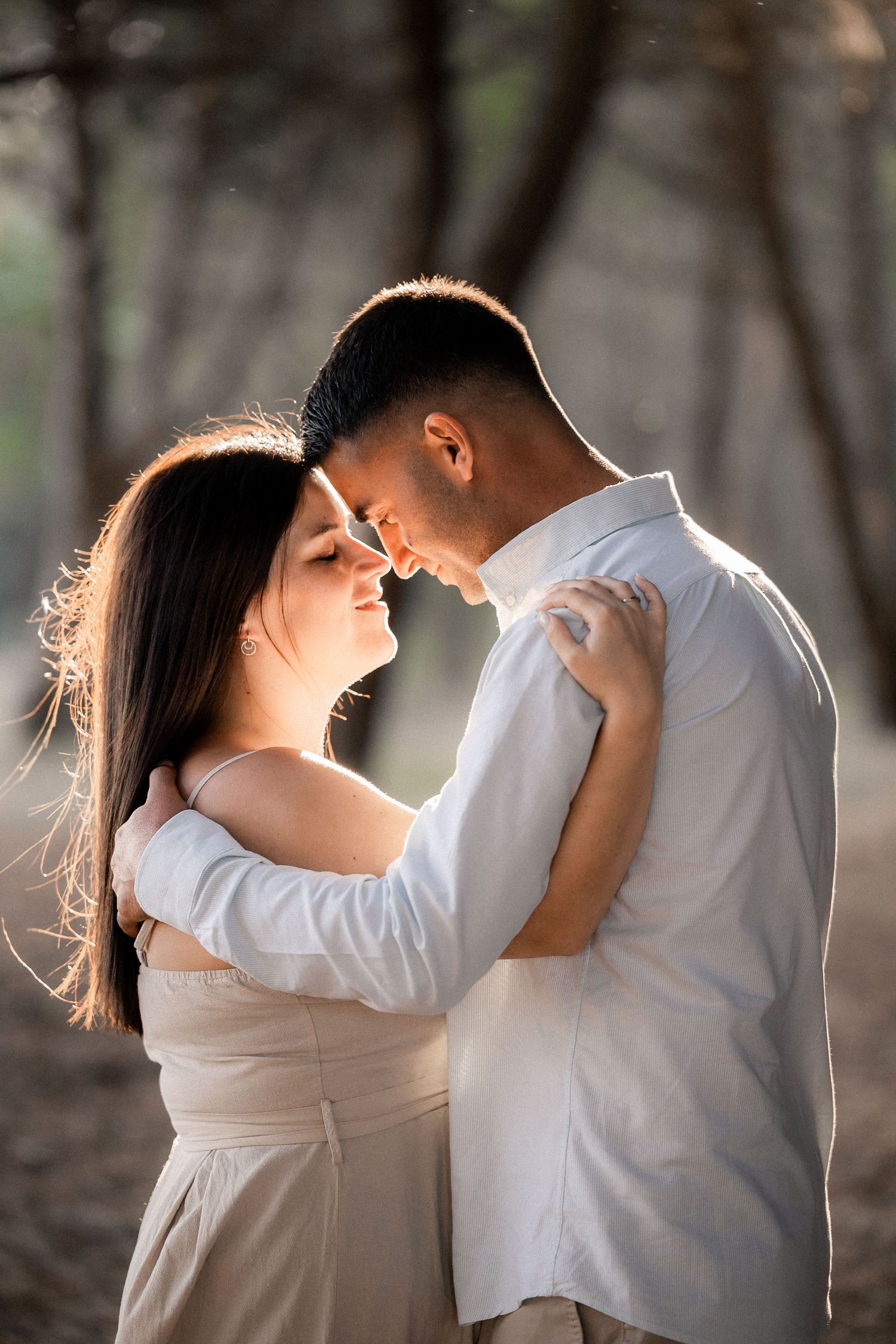 A romantic couple in white outfits share an intimate moment in soft backlit sunlight.