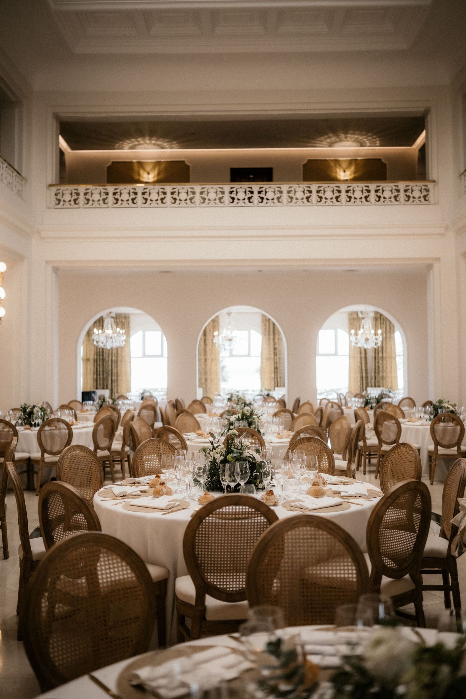 Elegant wedding reception venue with round tables, classic French chairs, and ornate crown molding details in sepia tones.