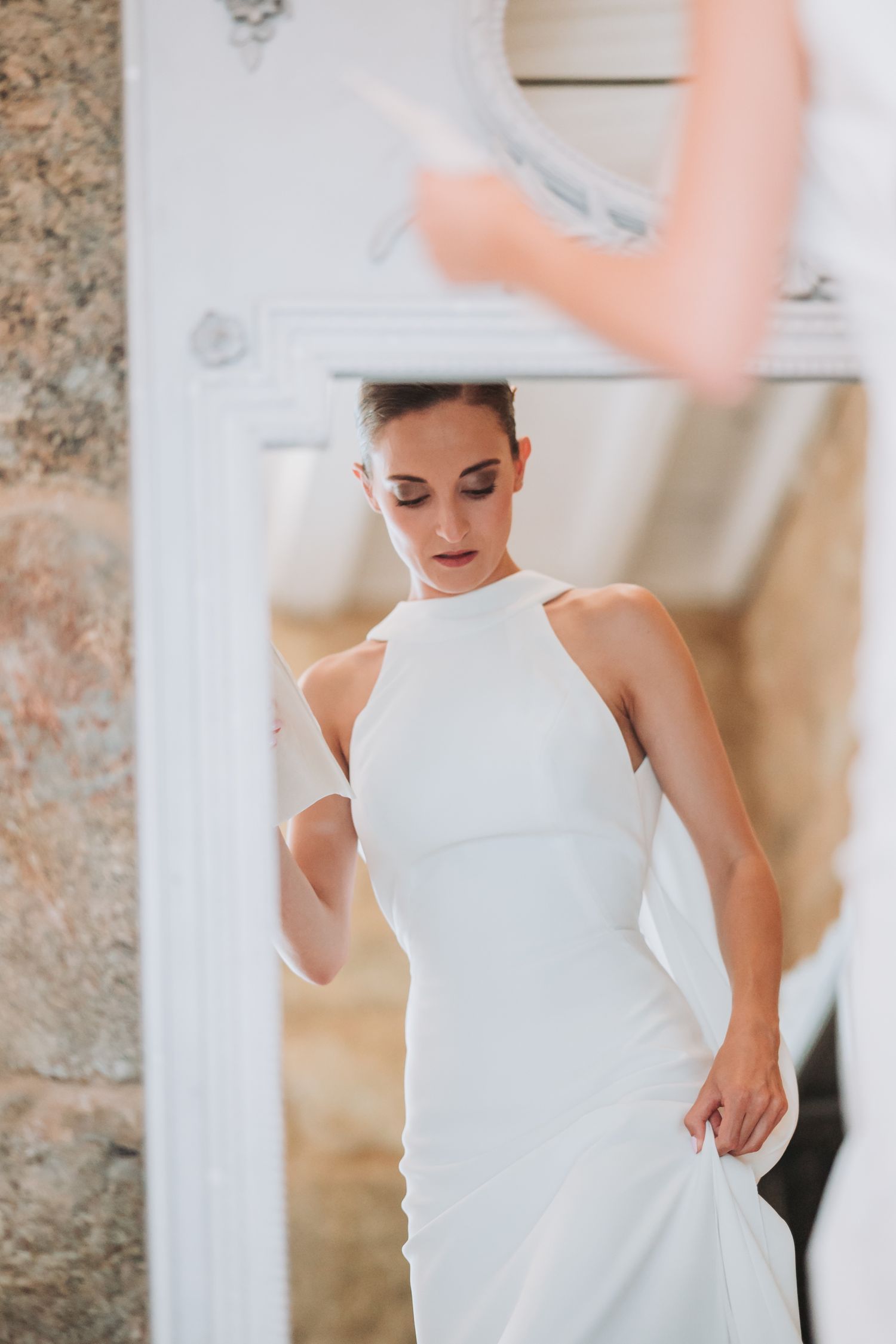 Elegant white wedding dress with sleek modern design shown in rustic stone interior.