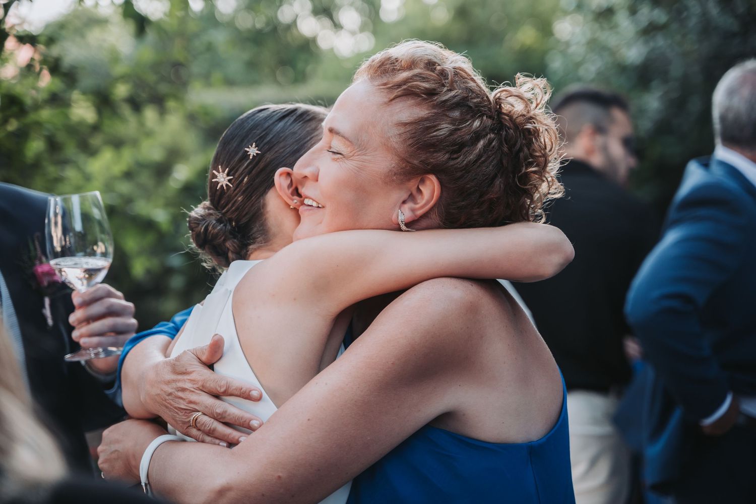 Wedding party members embrace and share emotional moments during an outdoor celebration.