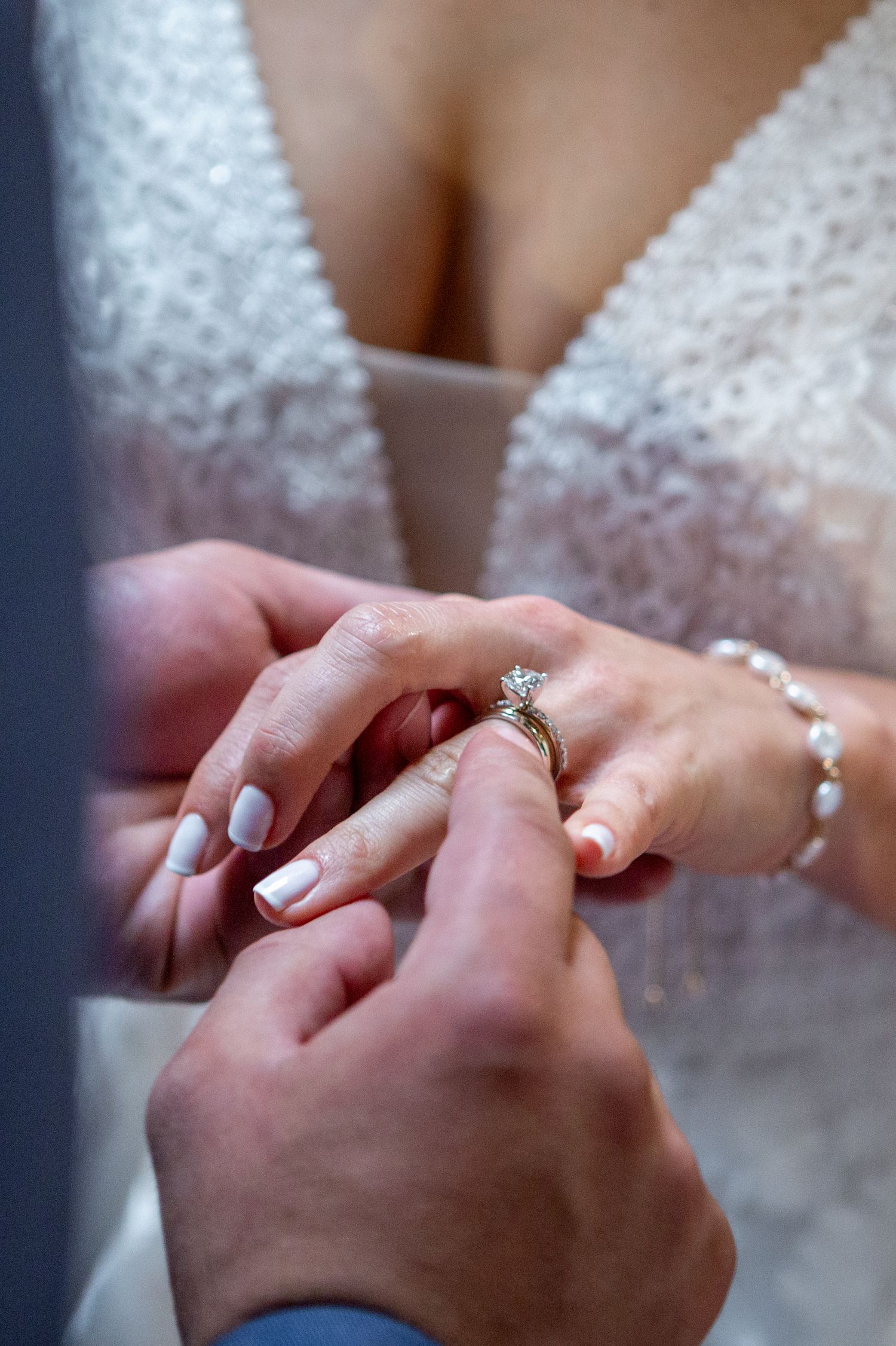 Close-up of hands exchanging wedding rings with sparkling diamond engagement ring visible.