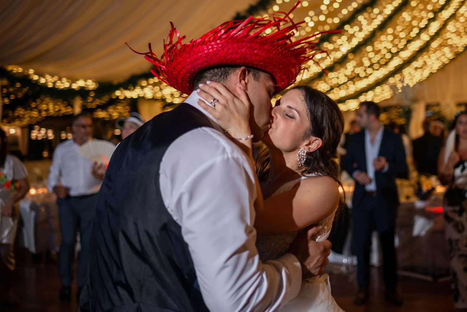 A couple shares a romantic dance moment under warm string lights at their wedding reception.
