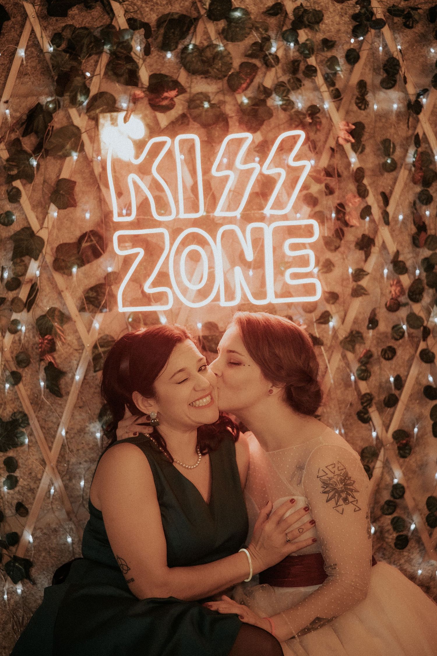 Two people share an intimate moment in front of illuminated neon signs and string lights.