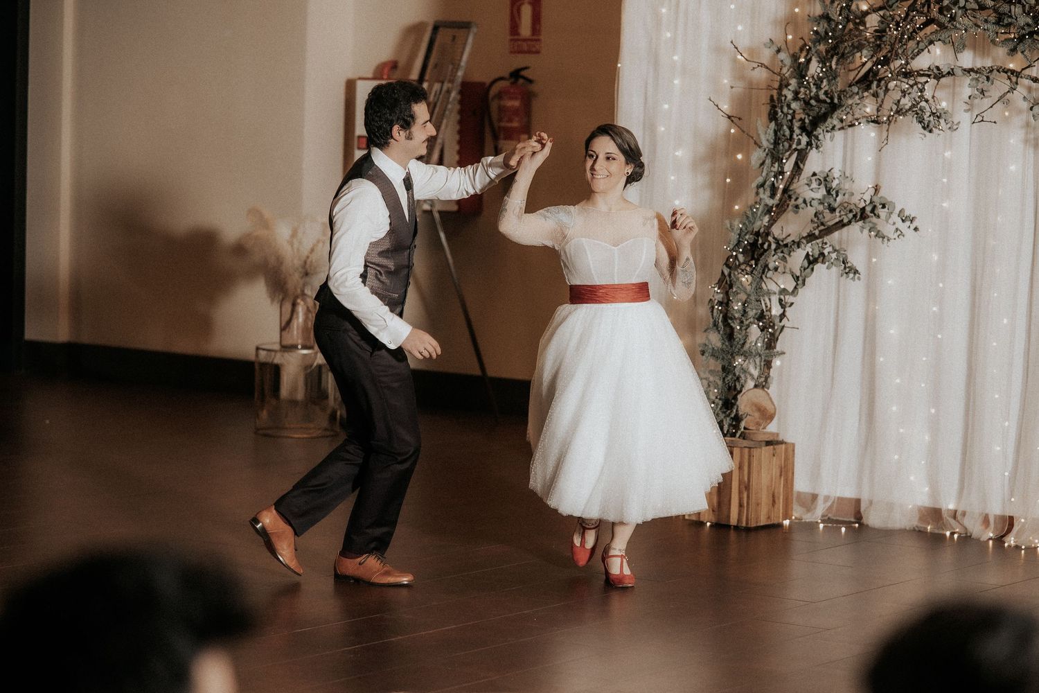 Two people share a joyful dance moment in a rustic indoor venue with soft lighting and natural decor.