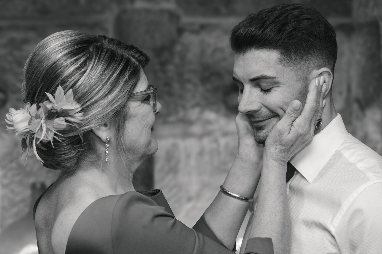Black and white photo of a couple sharing an intimate moment against a textured stone wall.