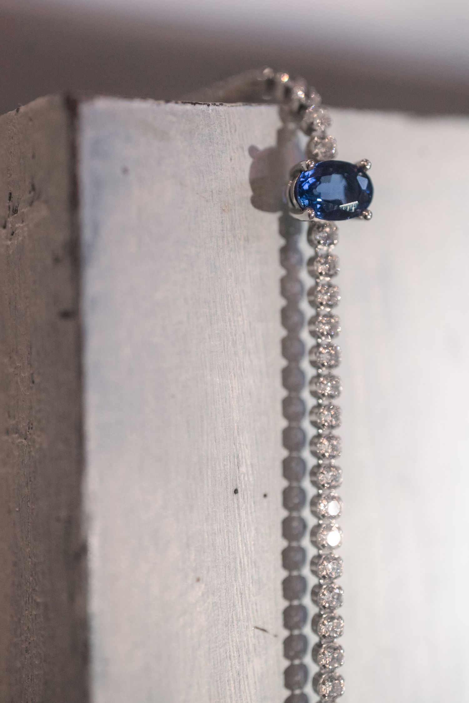 Elegant diamond tennis bracelet featuring a stunning blue sapphire centerpiece in white gold setting.