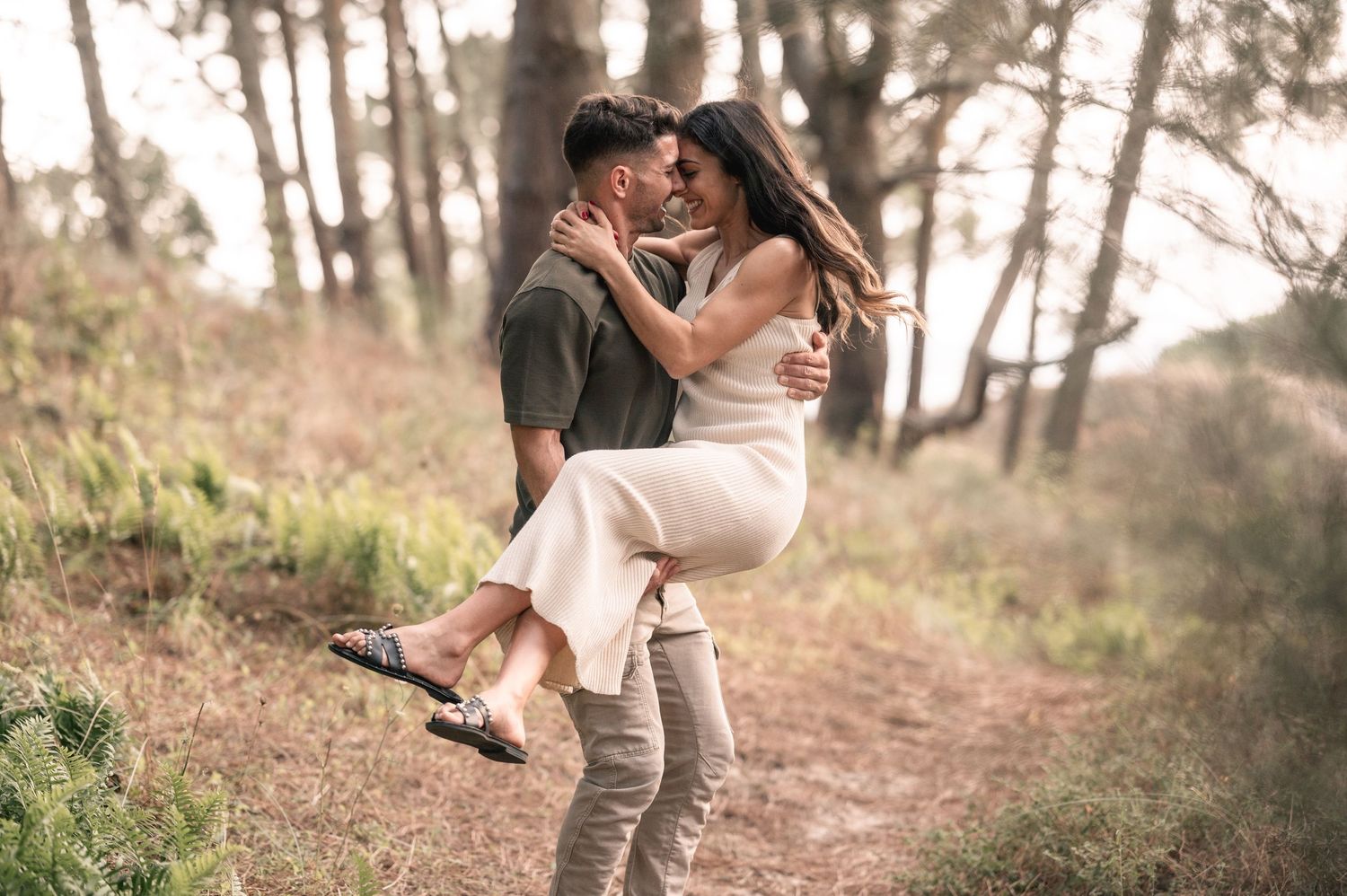 A romantic couple embraces on a sunlit forest trail during an outdoor photoshoot.
