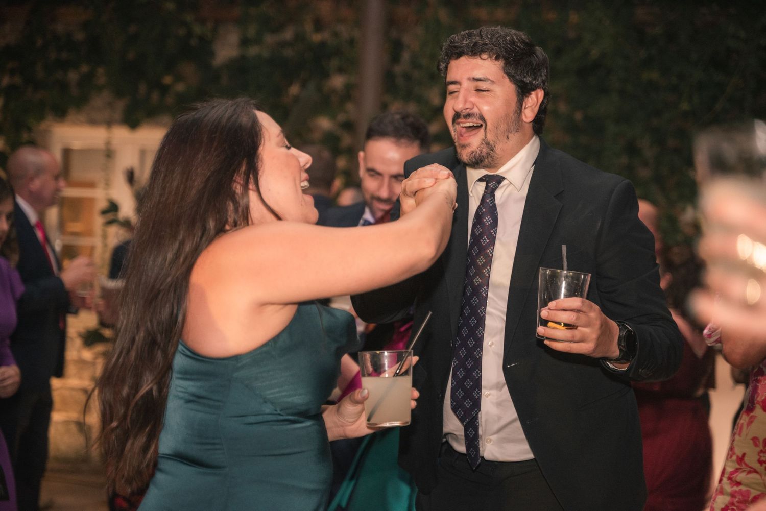 A couple shares a dance together at a wedding reception with other guests in the background.