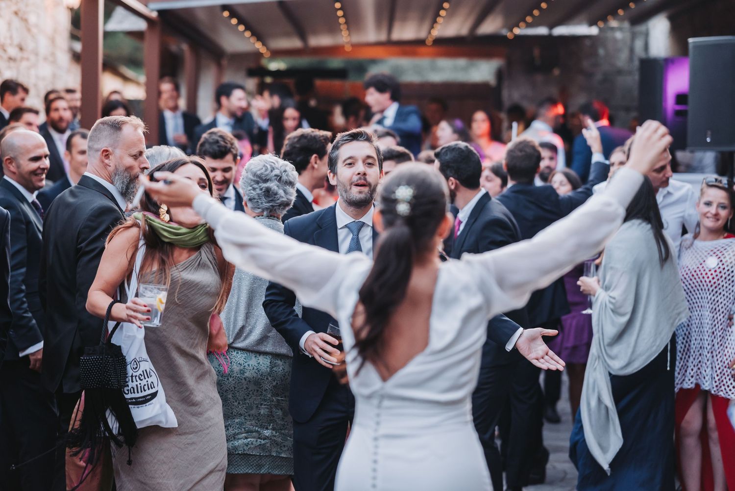 Wedding reception guests dance and laugh together during an energetic celebration indoors.