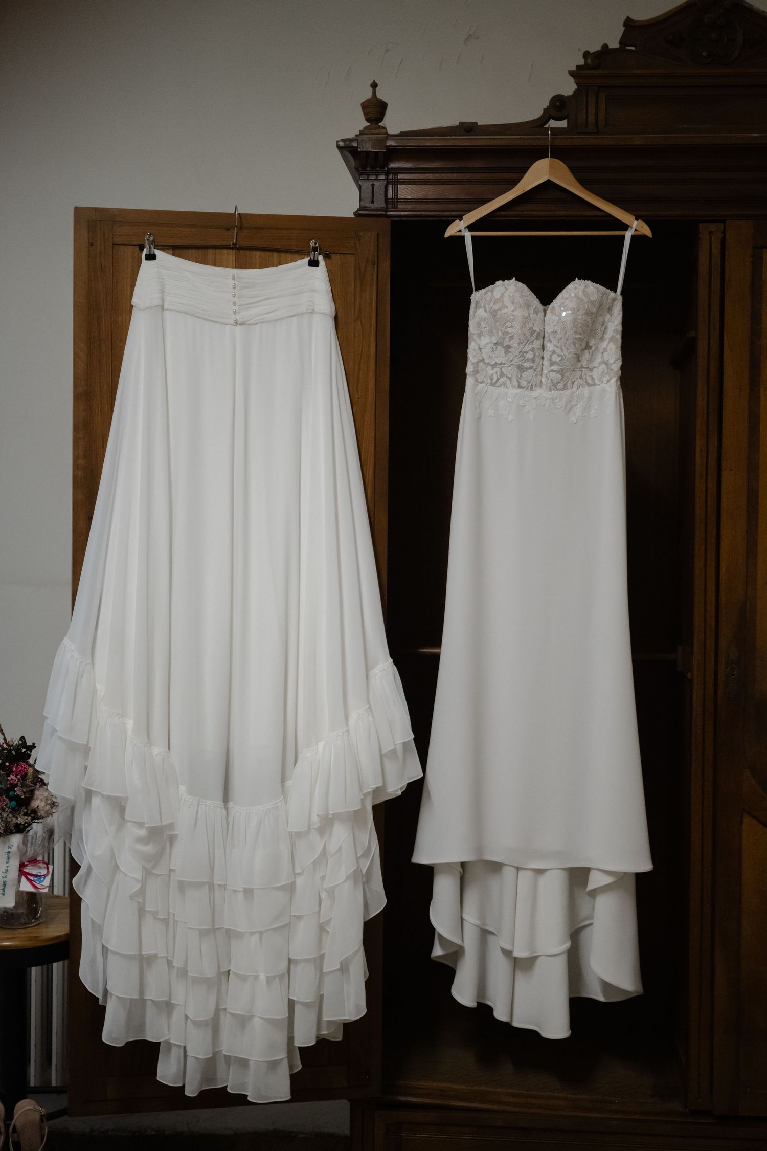 A white high-low layered chiffon skirt displayed on a hanger in different angles against a dark wooden backdrop.