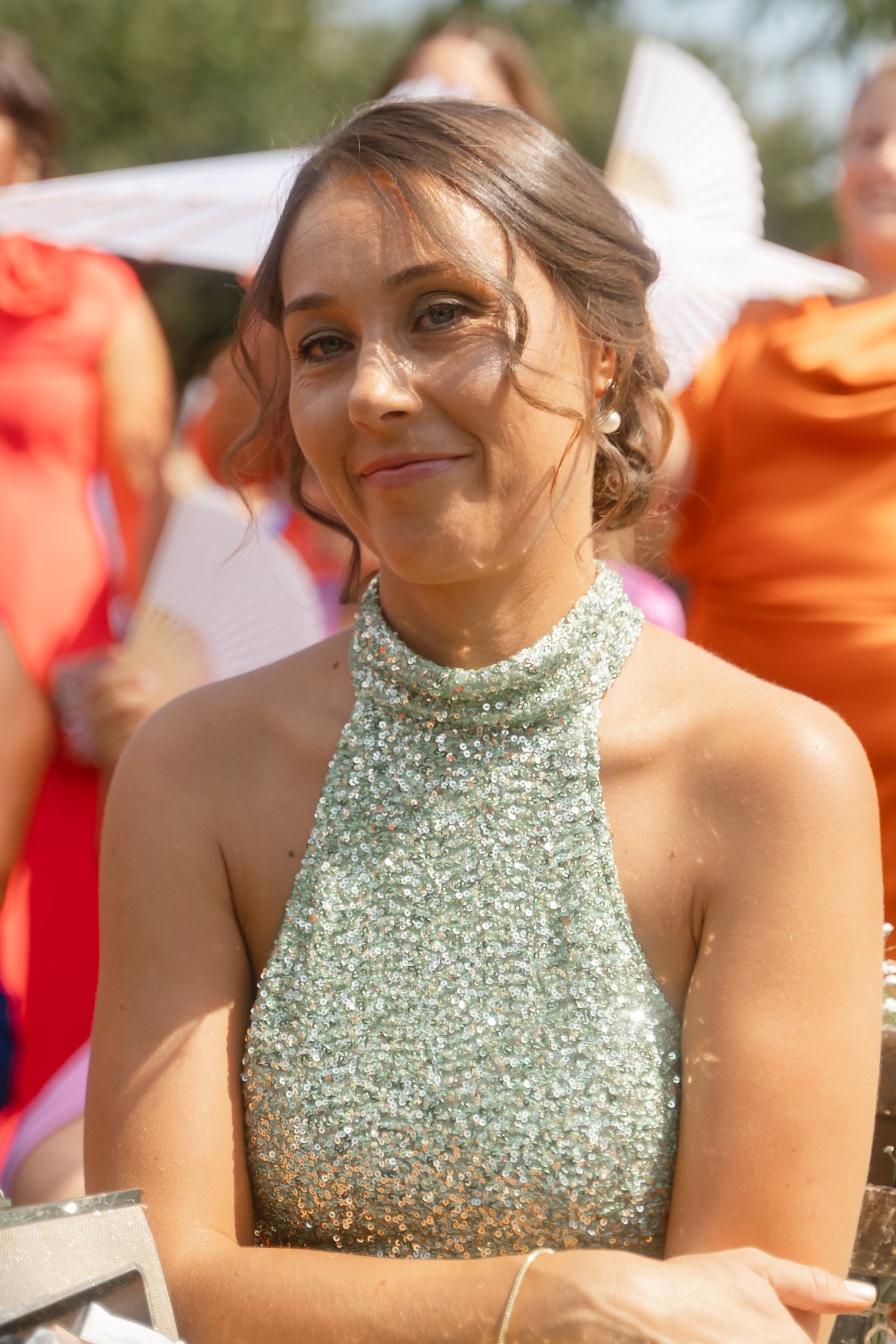 Woman in sparkling mint green halter dress smiles warmly at outdoor event on sunny day.