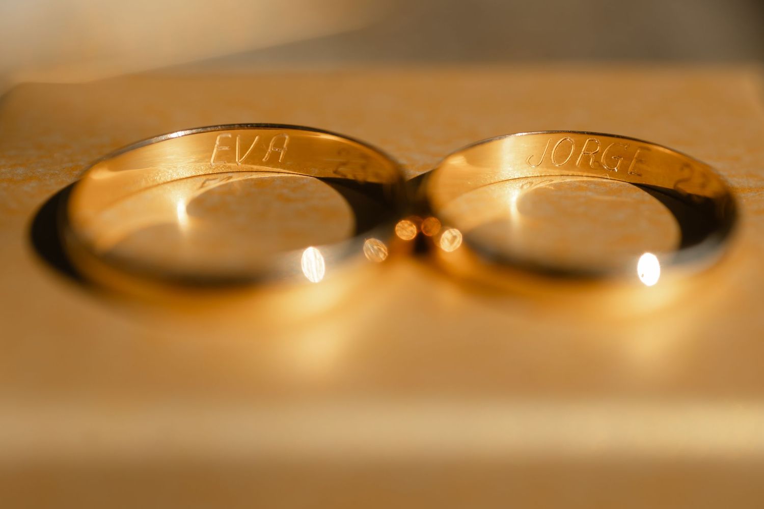 Close-up macro shots of golden wedding rings on a reflective surface in warm lighting.