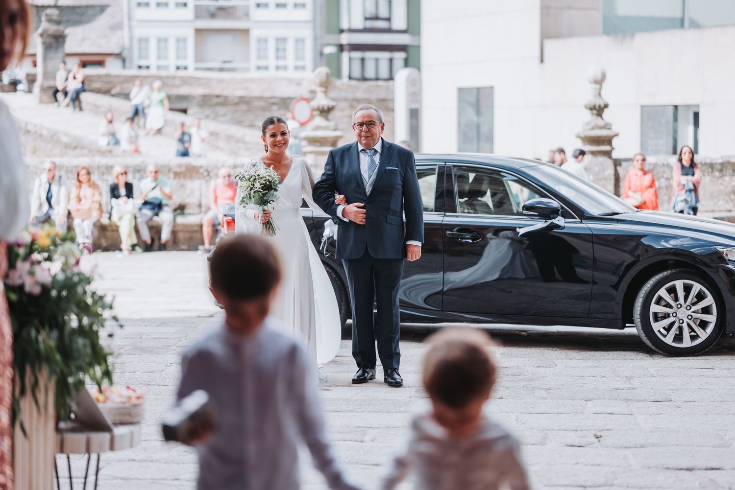 Elegant wedding party walks along a historic stone building exterior during a formal celebration.