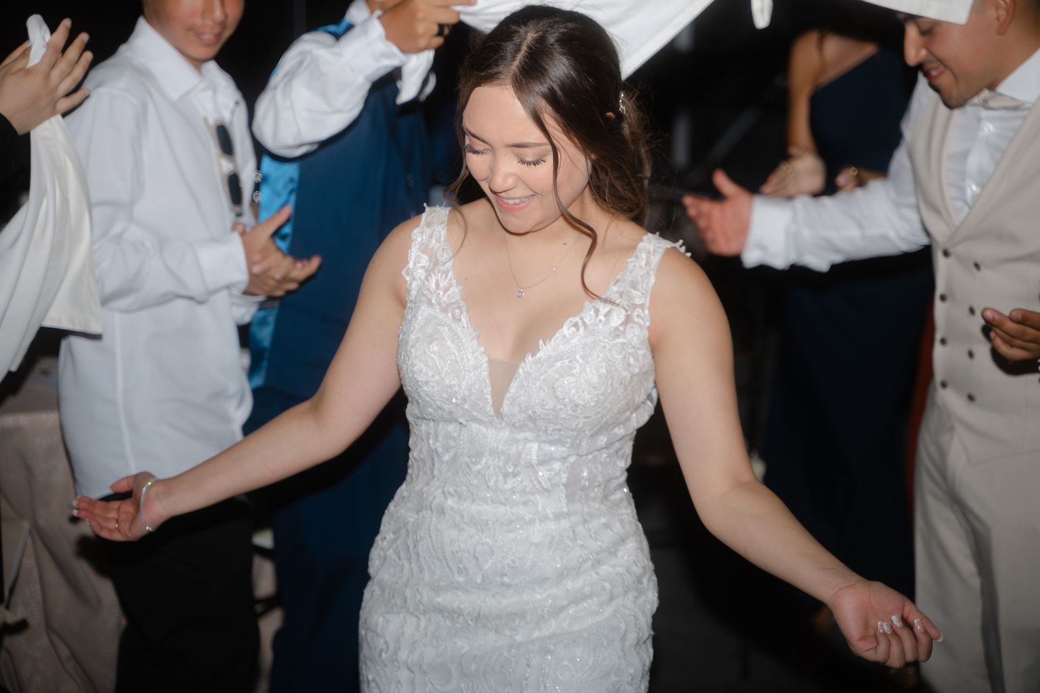 A person in a white lace wedding dress dances joyfully on a crowded dance floor at a reception.