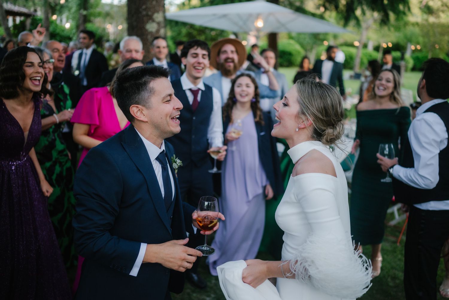 Wedding guests and newlyweds share joyful laughter during an outdoor garden reception.