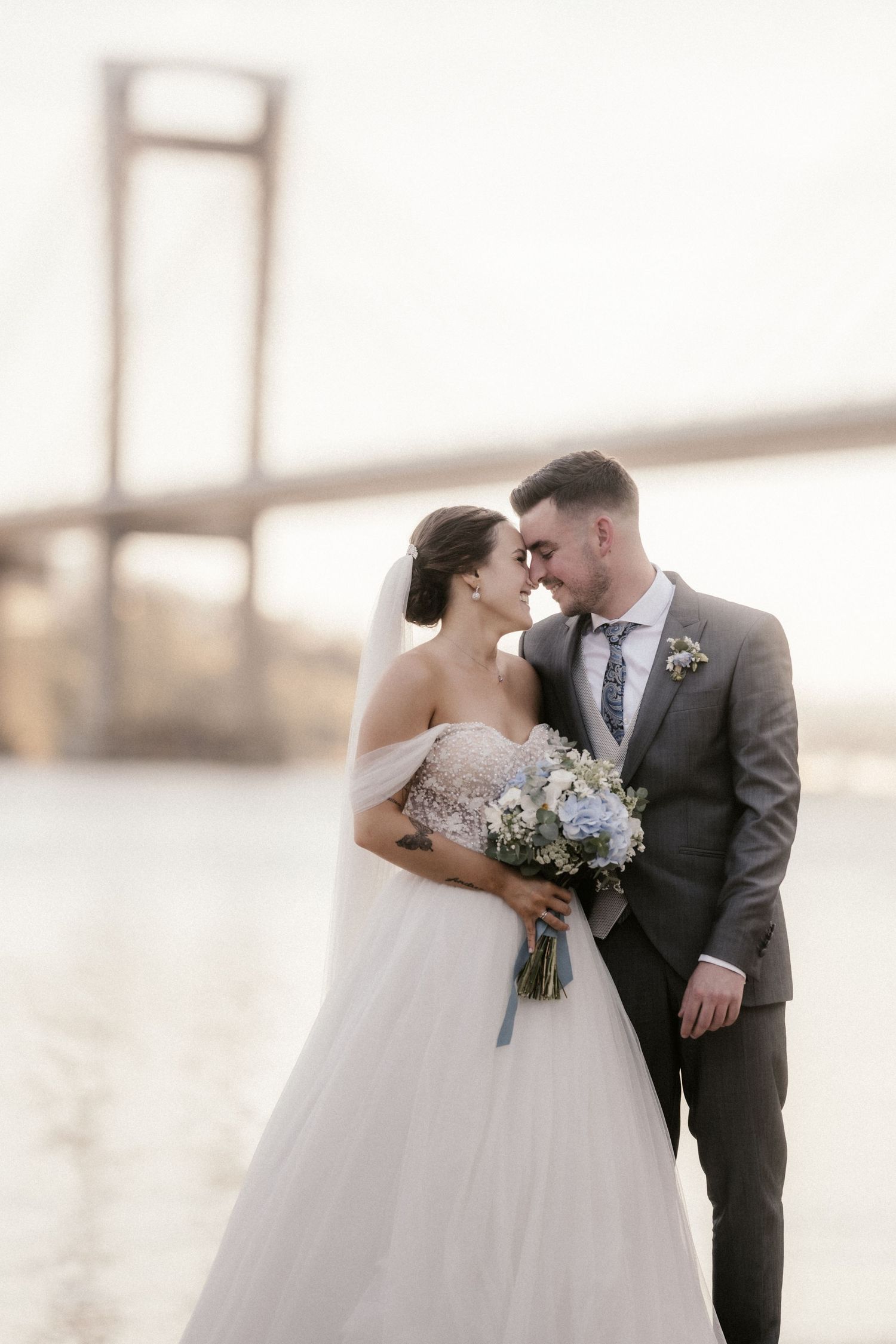 Romantic wedding couple shares a tender kiss at sunset with soft lighting and elegant attire.
