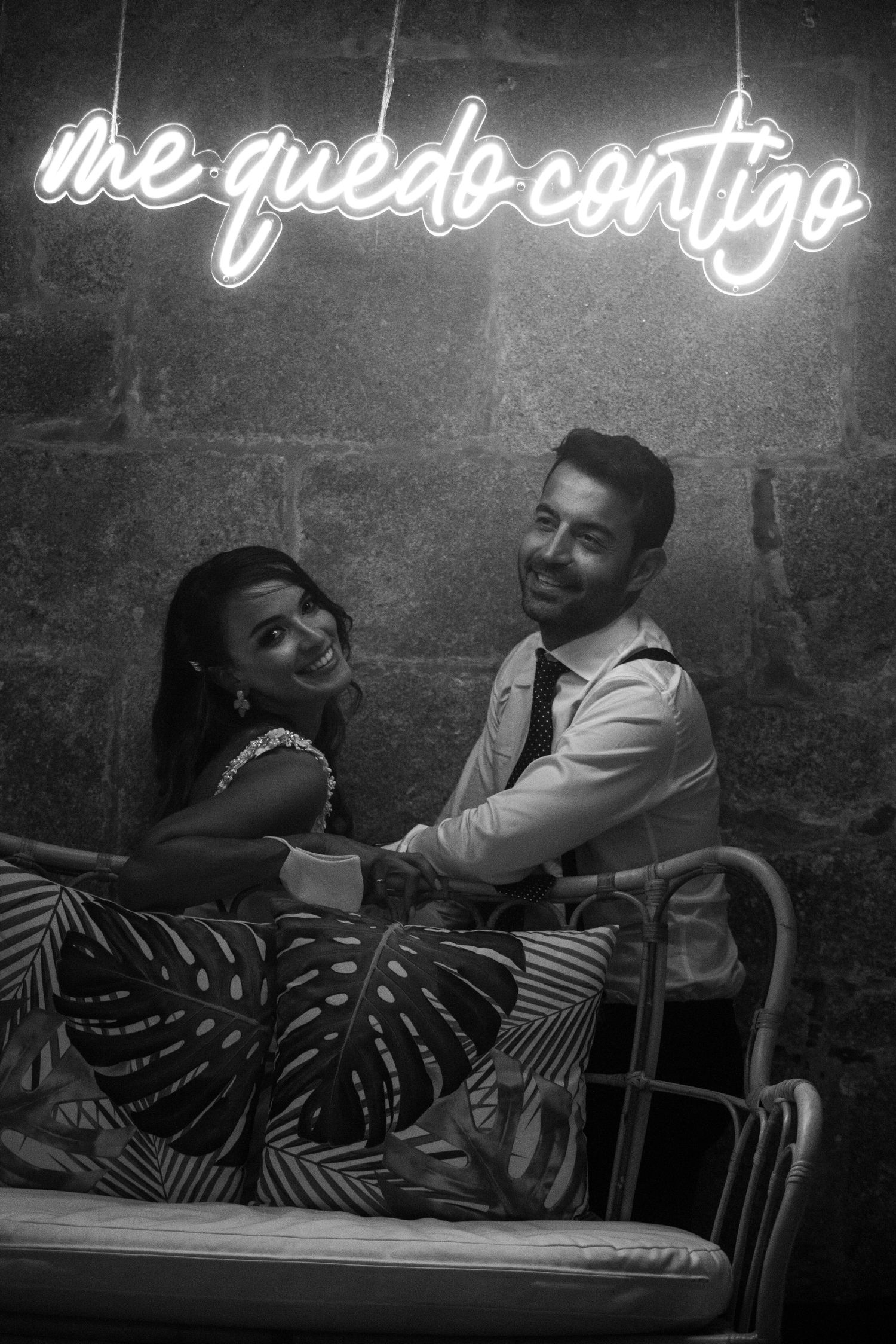 Black and white photos of a couple lounging beneath illuminated script text on a dark wall.