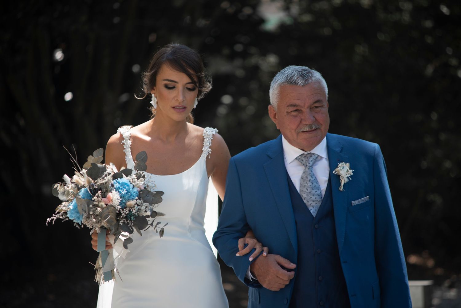 Elegant wedding ceremony outdoors with bride in white dress and groom in blue suit.
