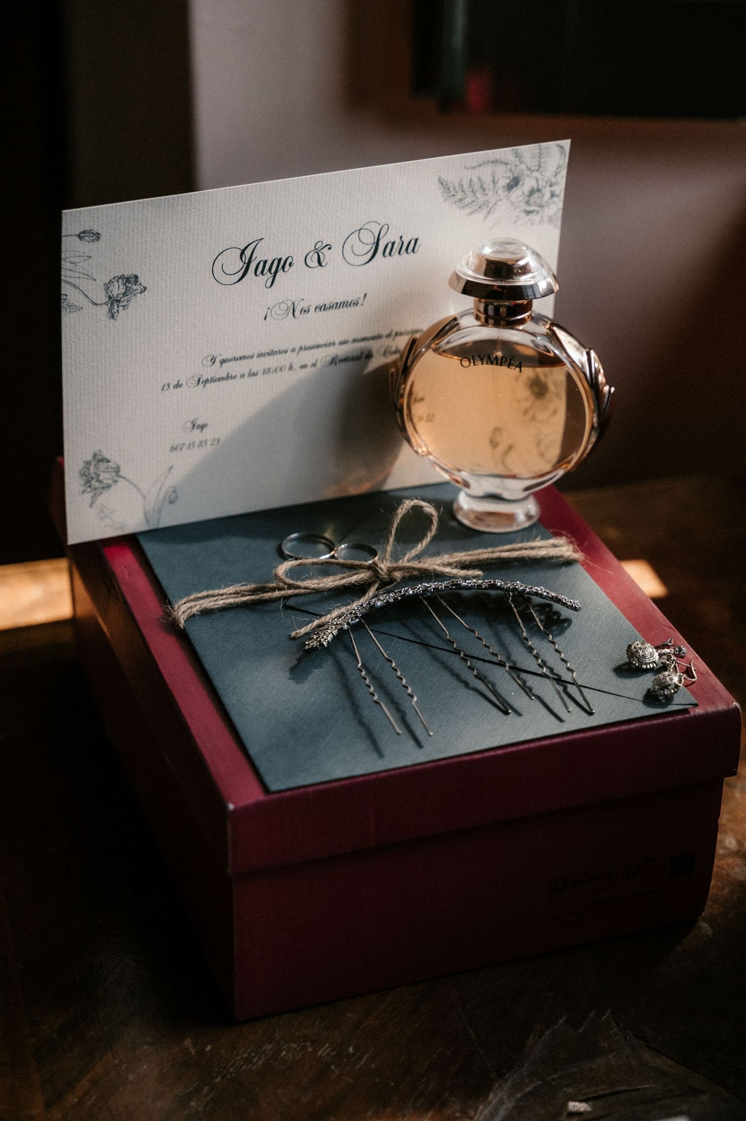 Elegant wedding invitation cards and decorative elements arranged on a dark burgundy surface in dramatic lighting.