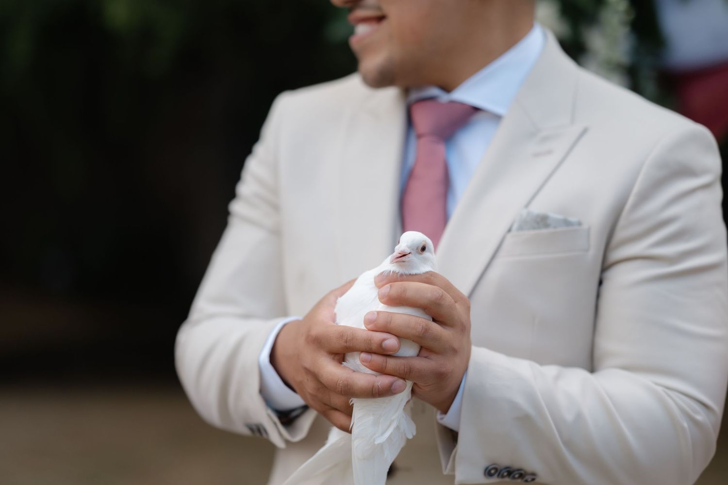 A close-up view of hands clasped together wearing a light beige suit jacket with a pink tie.