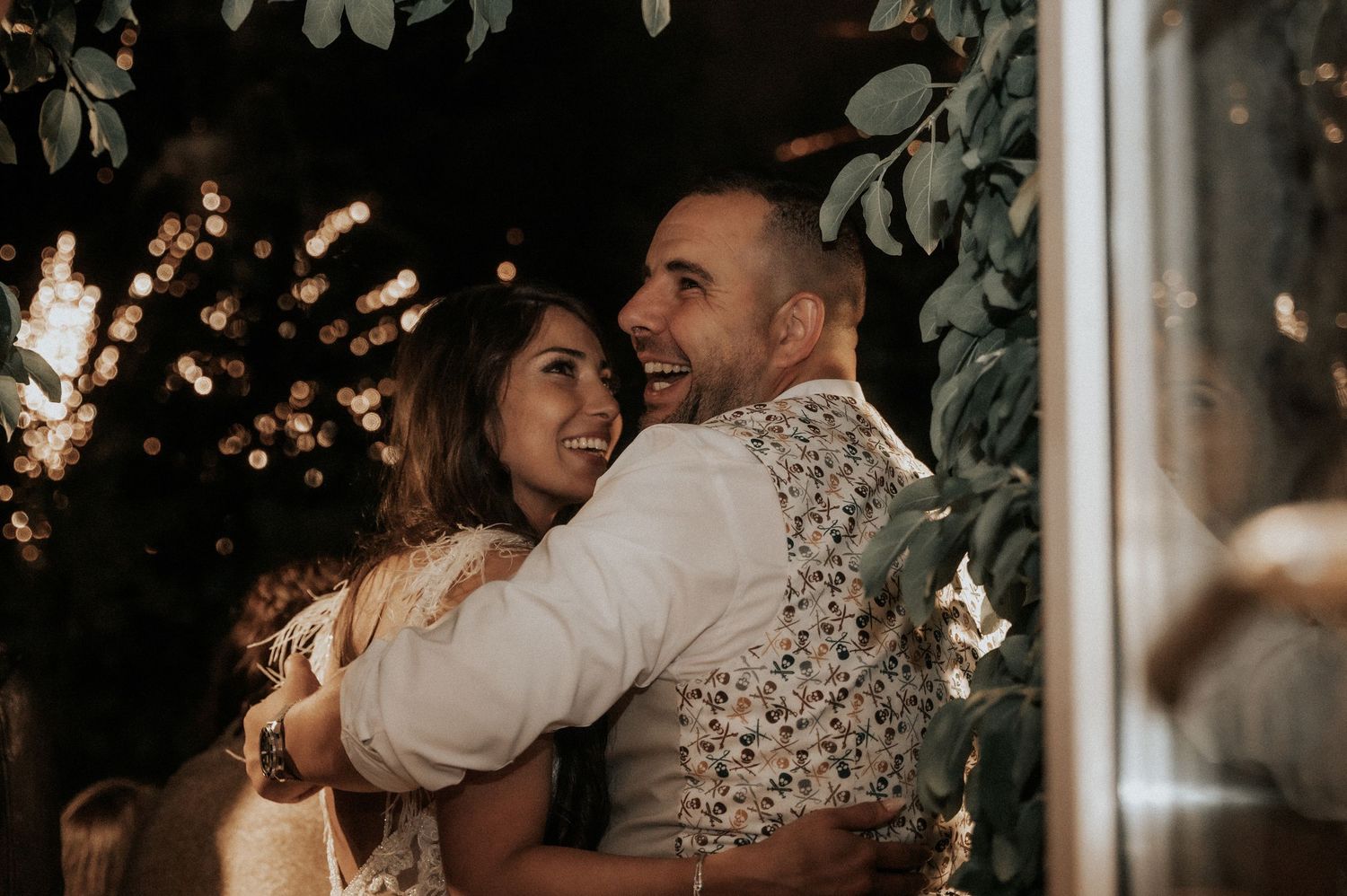A couple embraces while dancing at a romantic evening celebration with twinkling lights in the background.