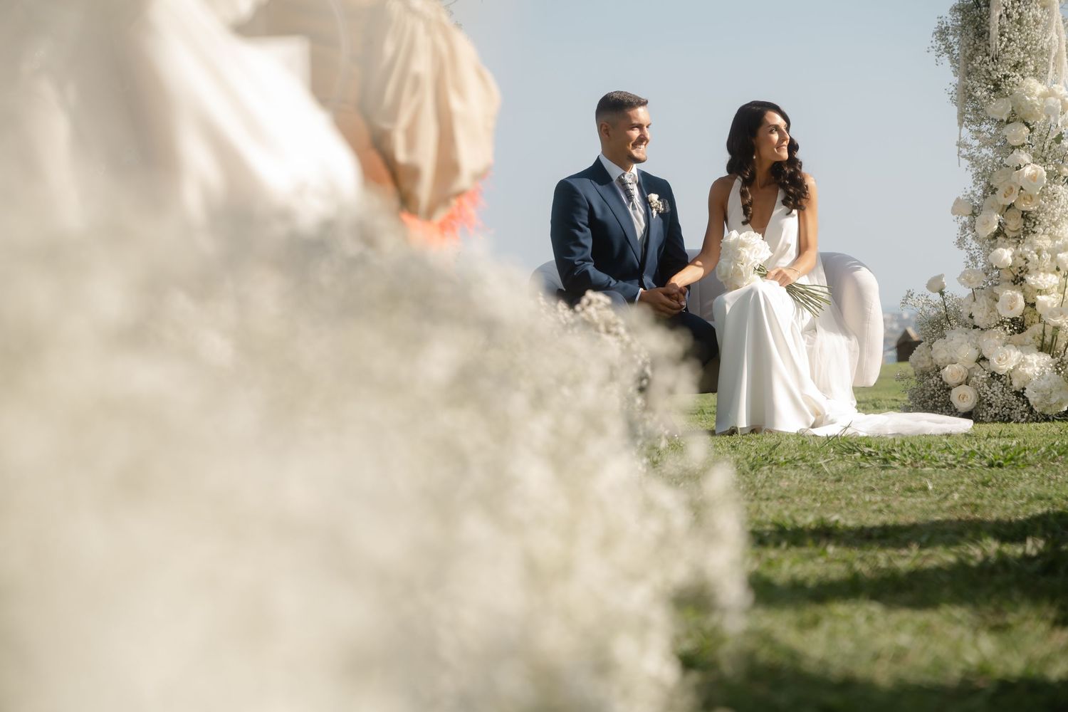 Elegant outdoor wedding scene with white floral decorations and natural coastal scenery in the background.