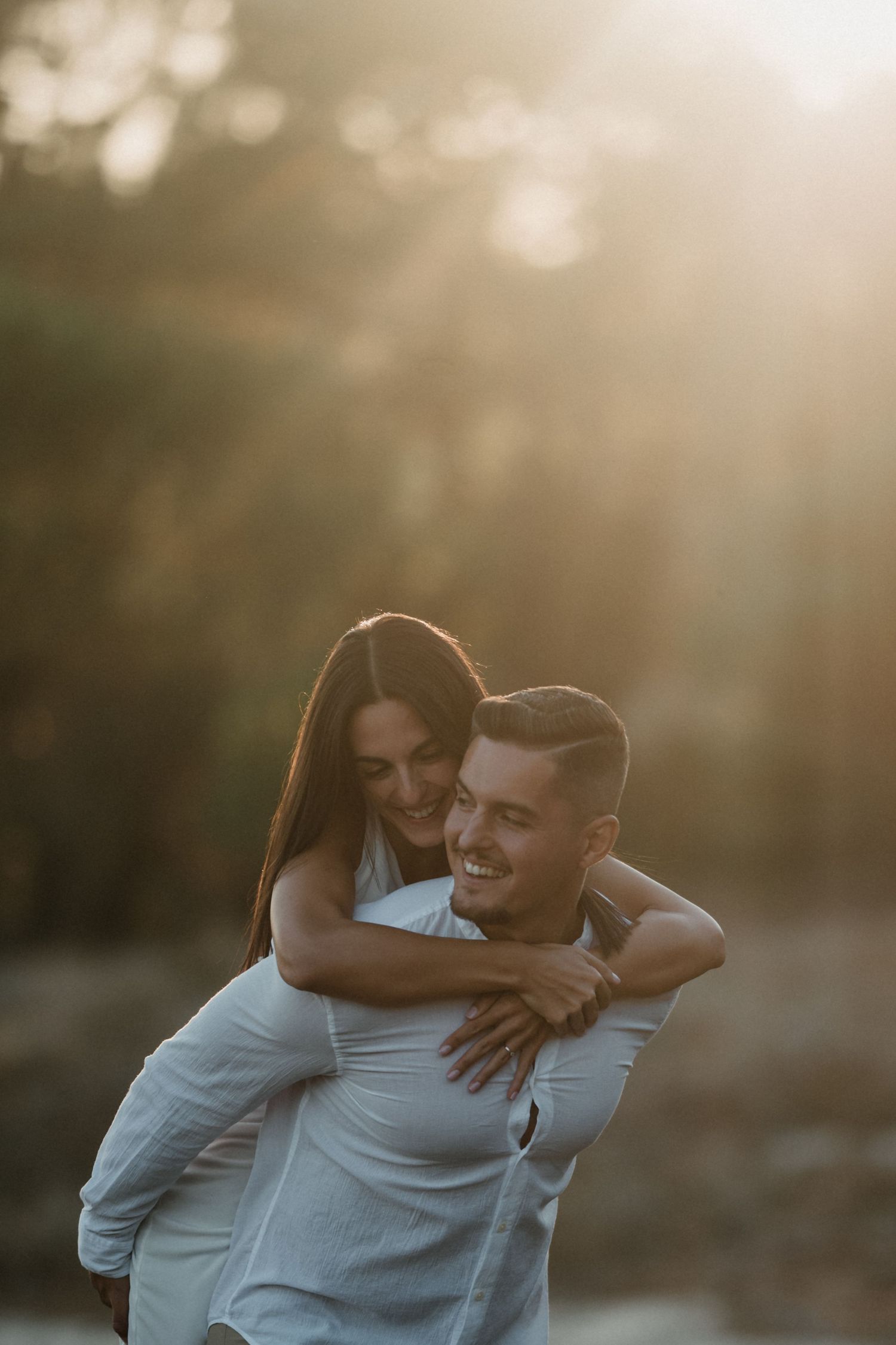 A couple embraces in a warm sunset glow, sharing an intimate moment against a softly blurred background.