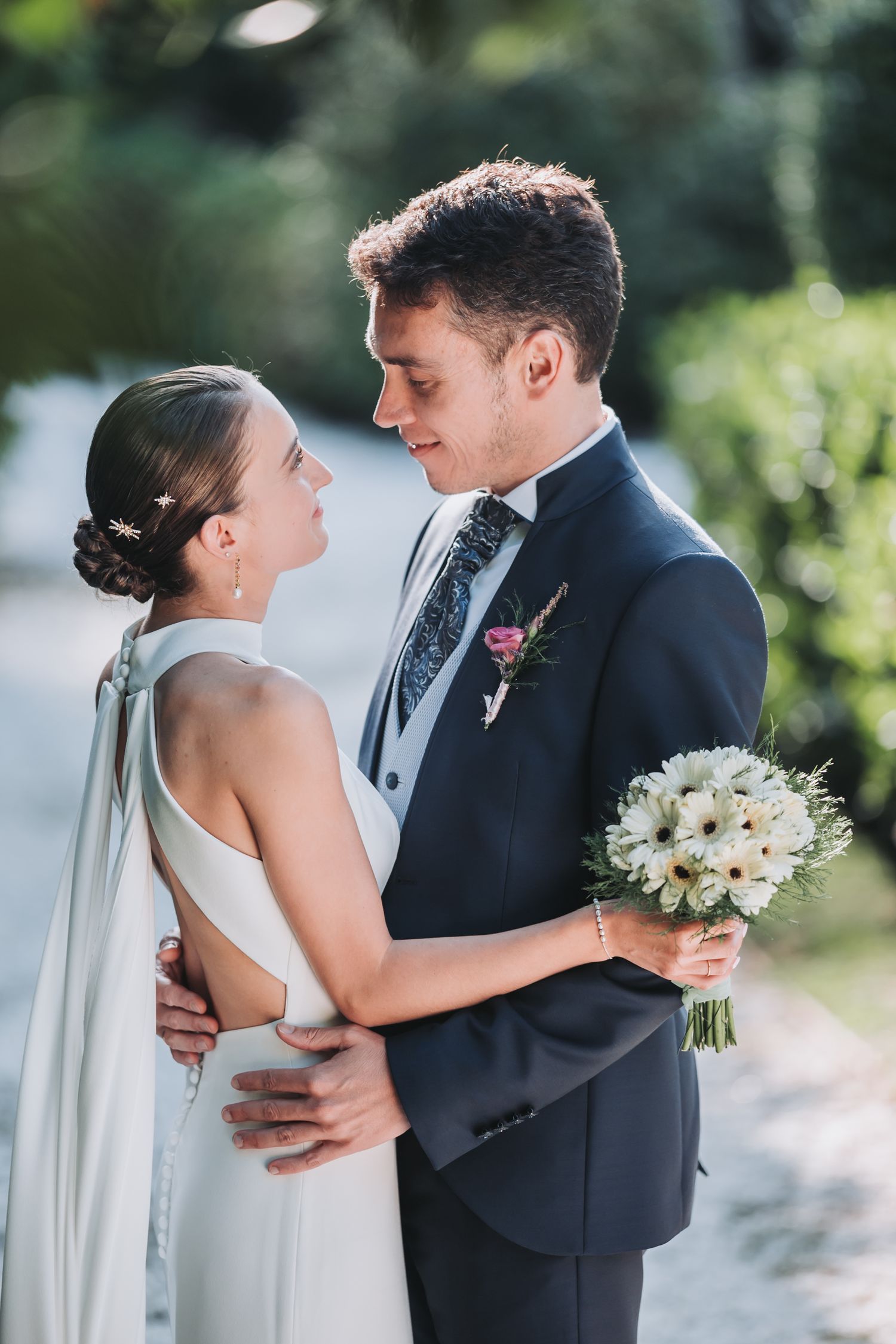 Romantic wedding couple shares intimate moments in a garden setting with white flowers and elegant attire.
