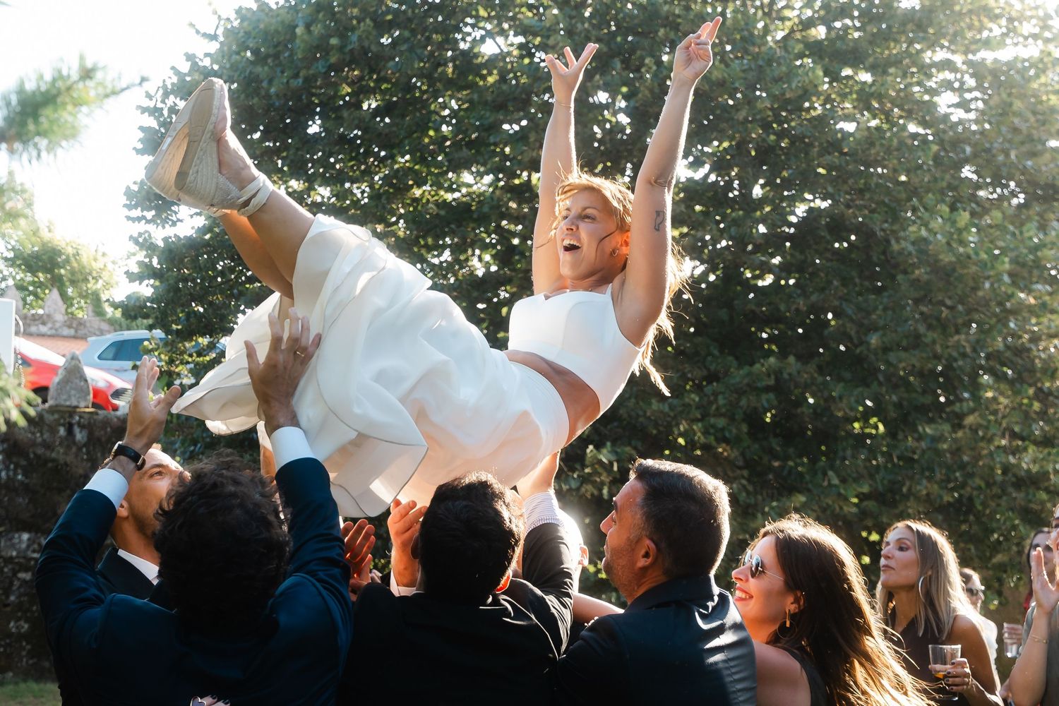 A crowd of wedding guests cheering and raising their hands in celebration during an outdoor ceremony.