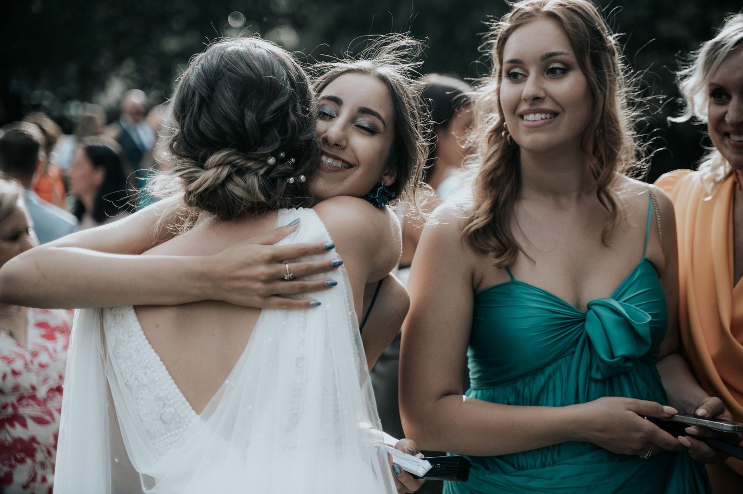 Wedding party members in teal and peach dresses share joyful moments during outdoor celebration.