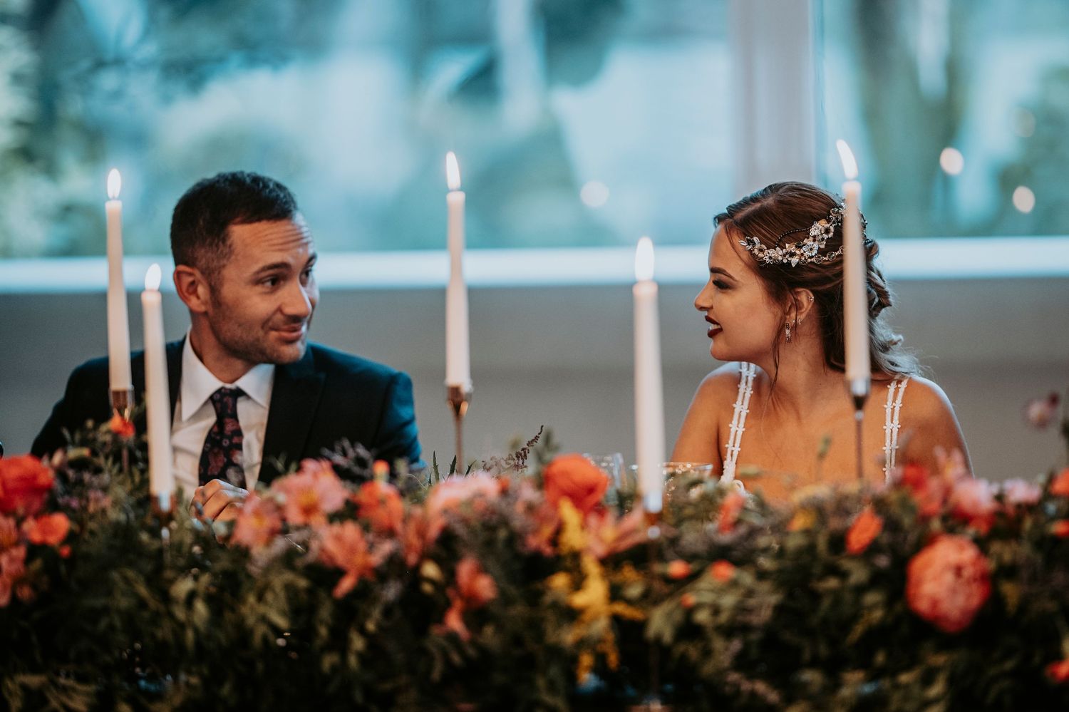A couple shares a joyful moment during their wedding reception with candlelit tables and floral arrangements in the background.