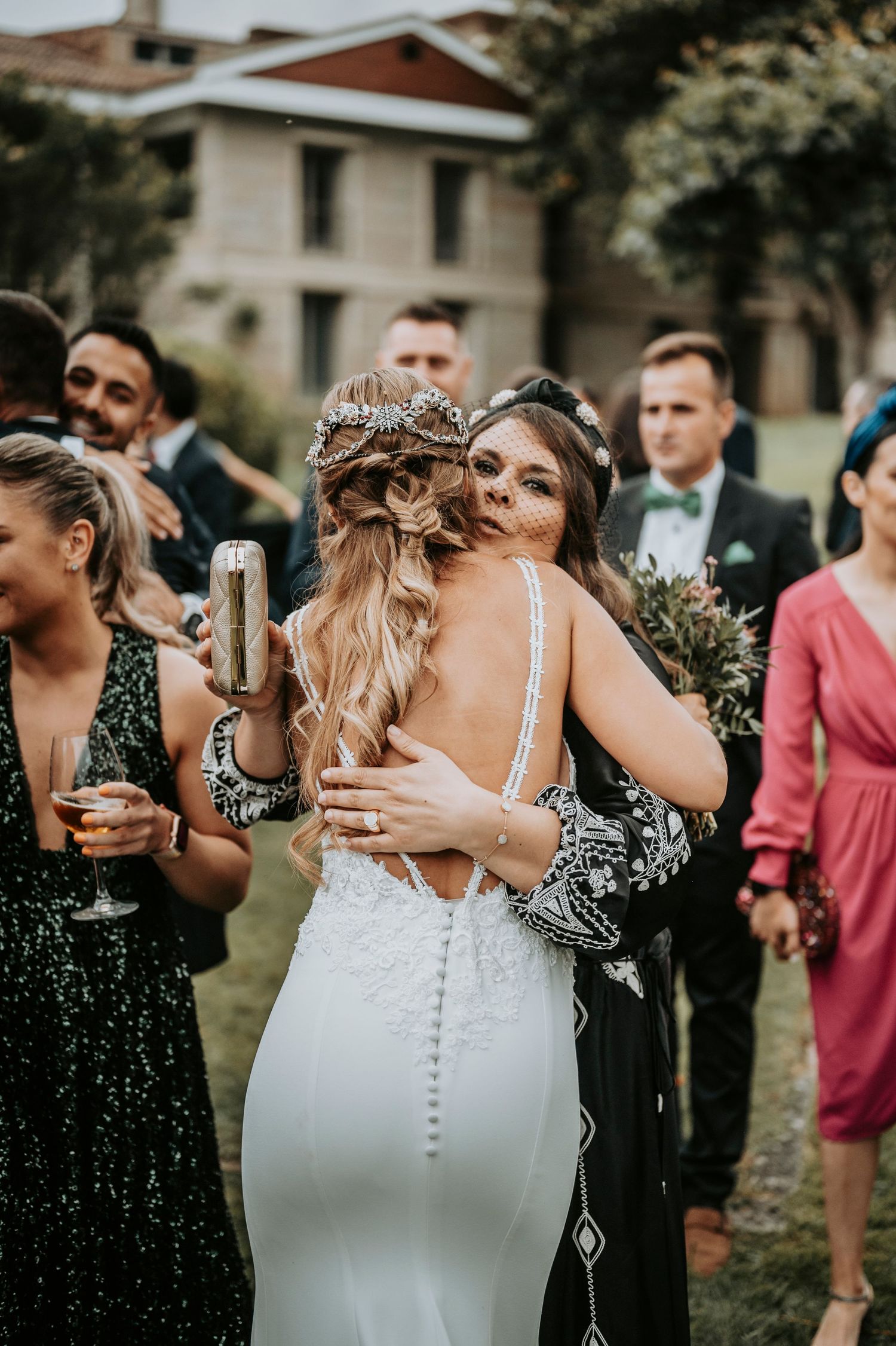 Wedding guests gather outdoors for a celebration with people embracing and socializing.