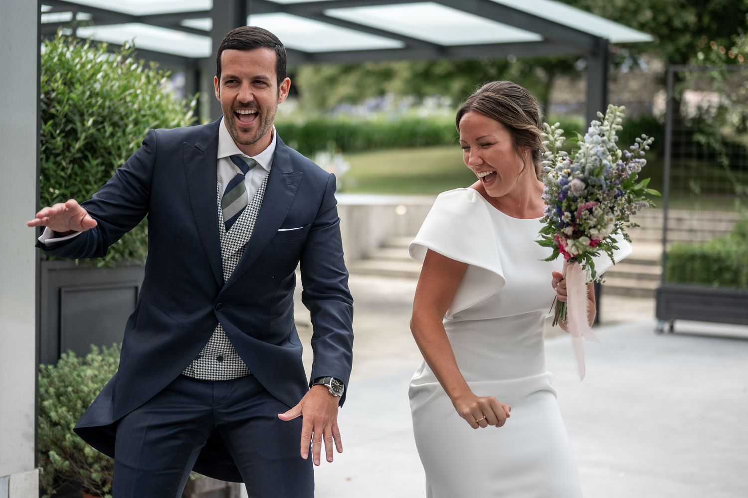 A joyful wedding couple shares candid moments outdoors in a garden setting during their special day.